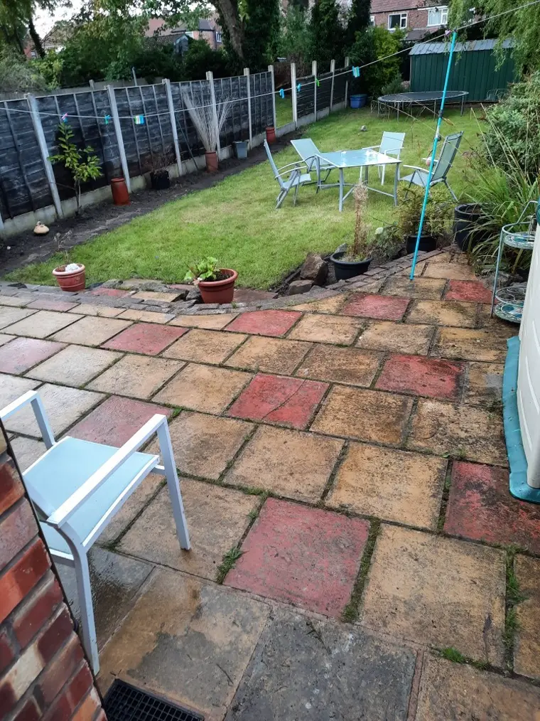 A tidy buff and red flagstone patio with a freshly mown back lawn, garden table and chairs
