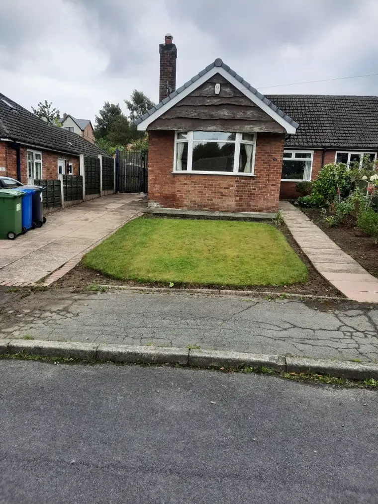 A neat front garden of a brick bungalow with a trimmed green lawn and tidy driveway