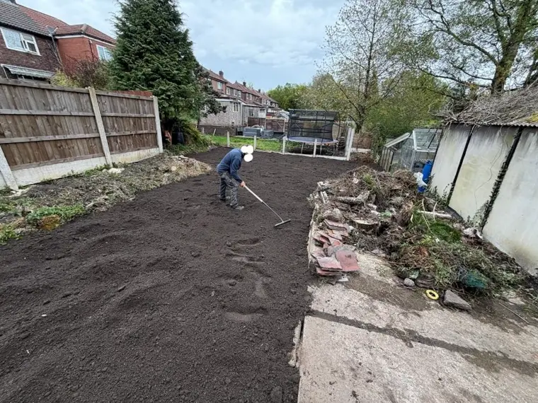 Fresh dark topsoil being raked and levelled in a back garden to prepare for a new lawn